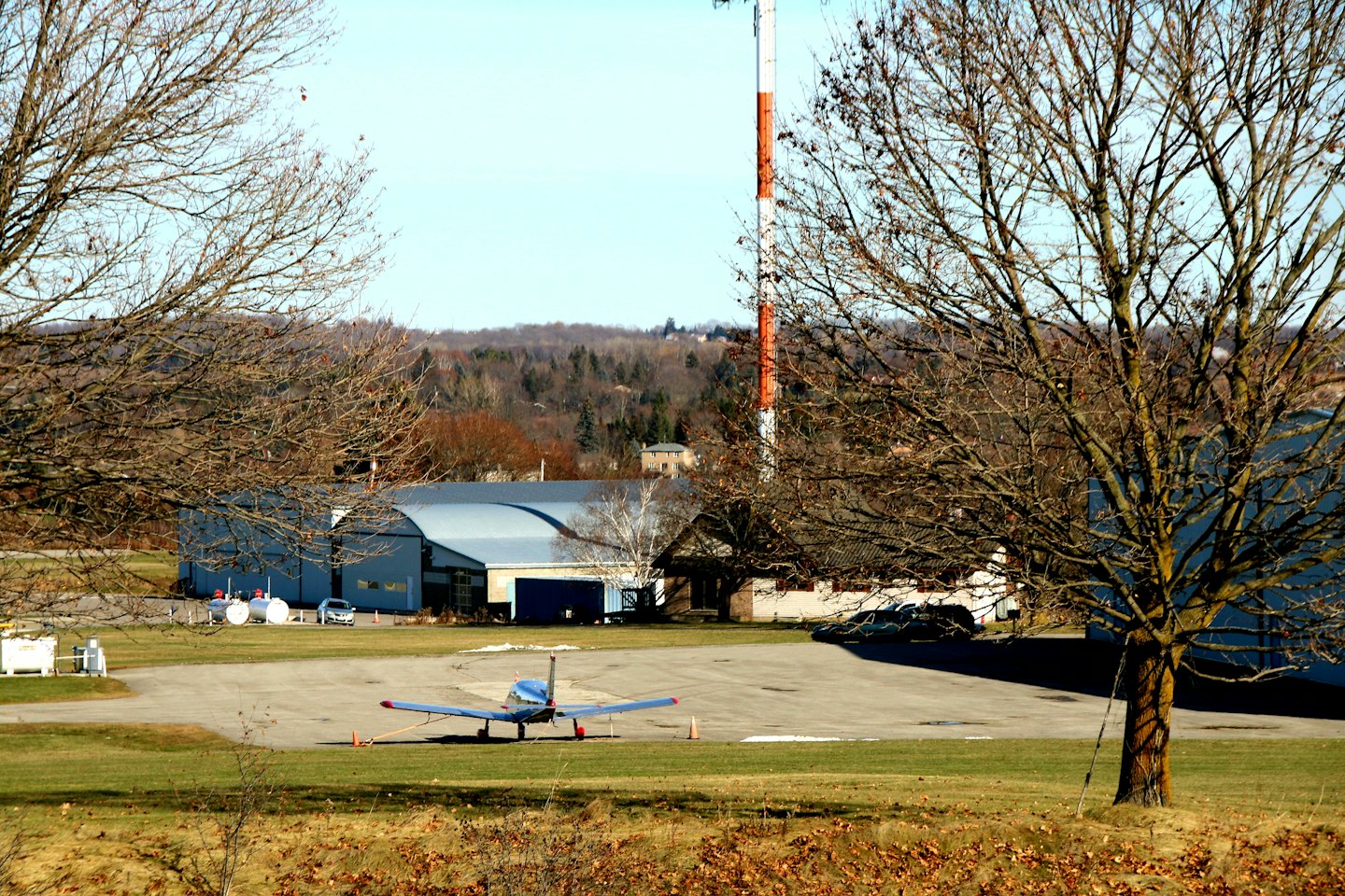 Piccolo aereo parcheggiato sulla pista di un aerodromo vicino agli hangar.