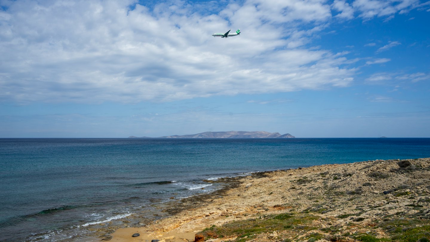 Un aereo sorvola una costa rocciosa e un mare blu-verde.
