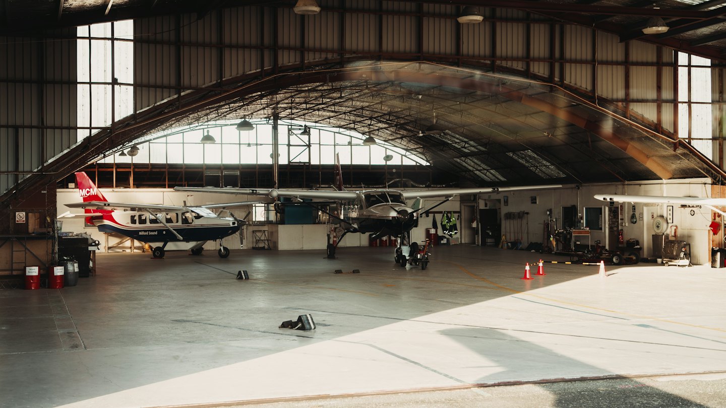 Due piccoli aerei parcheggiati all'interno di un grande hangar metallico.