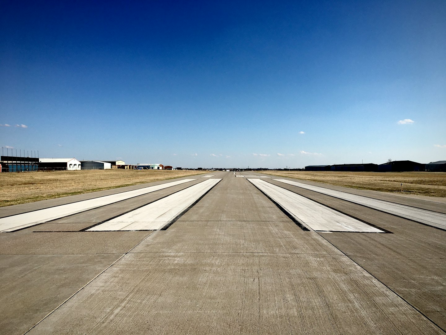 Pista dell'aeroporto in cemento con segnaletica bianca sotto un cielo blu.